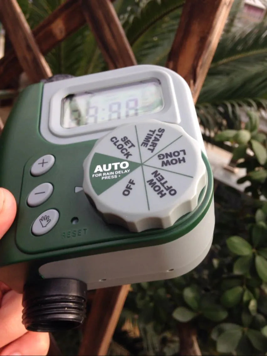 Green programmable digital garden hose timer with dual outlets and large LCD display connected to a faucet.