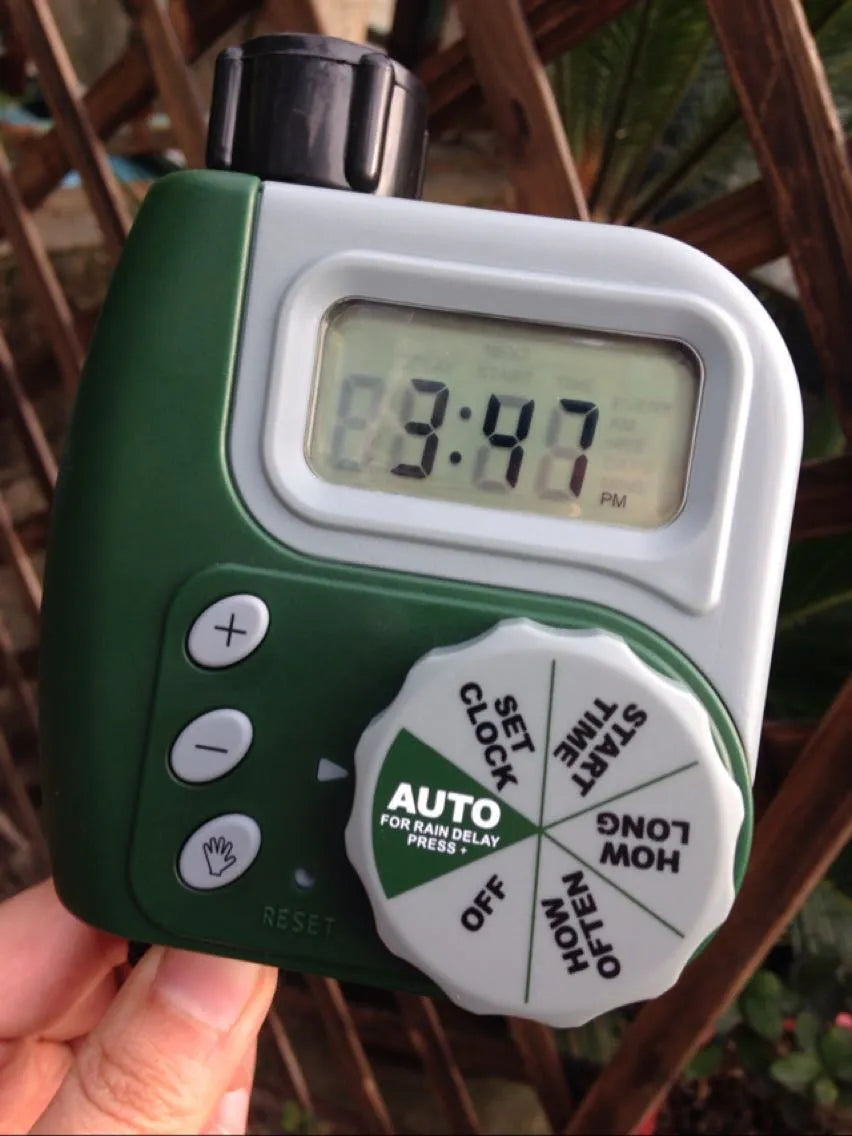 Green programmable digital garden hose timer with dual outlets and large LCD display connected to a faucet.