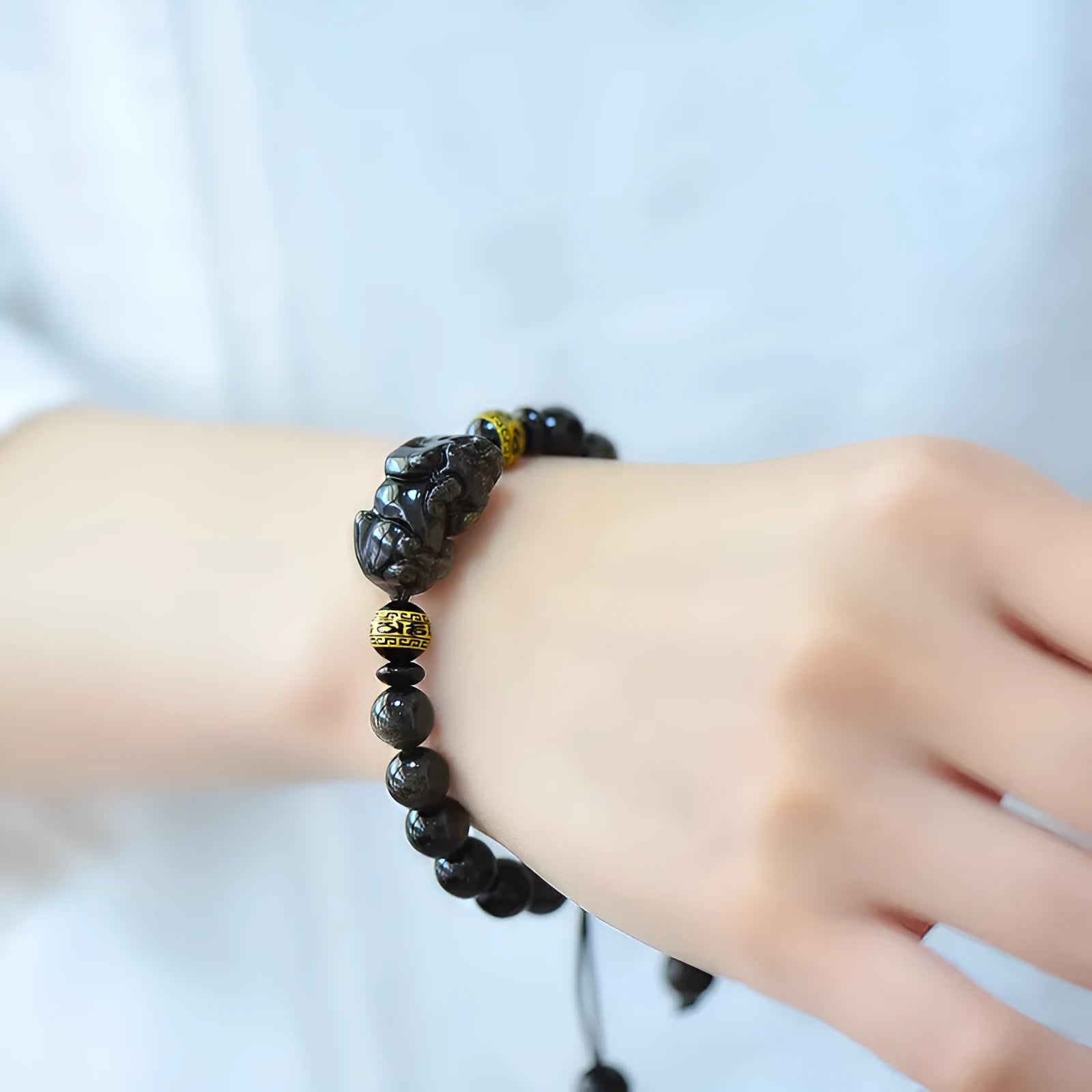 Close-up of a black obsidian bead bracelet with a detailed silver Pi Xiu charm on a neutral background.