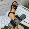 Women's flat black sandals with flip-toe design, ankle buckle, and cross-strap.