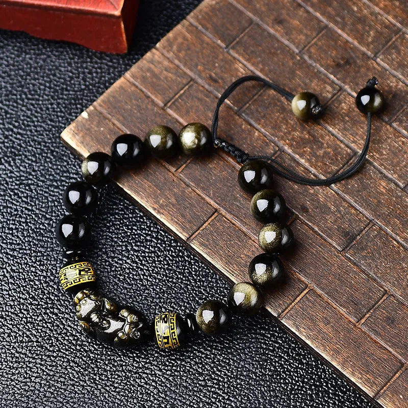Close-up of a black obsidian bead bracelet with a detailed silver Pi Xiu charm on a neutral background.