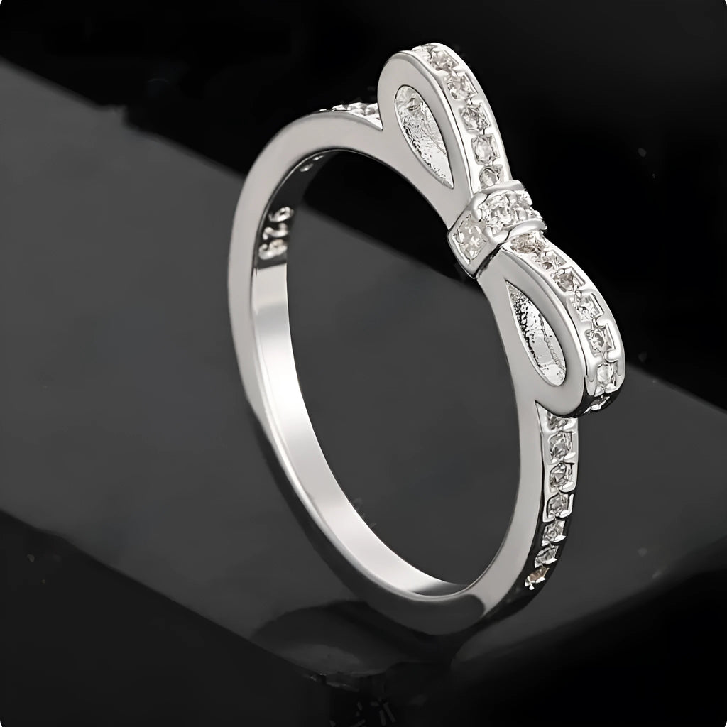 Silver coloured bow-shaped ring with rhinestone and zircon crystal details on a model finger.
