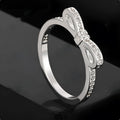 Silver coloured bow-shaped ring with rhinestone and zircon crystal details on a model finger.
