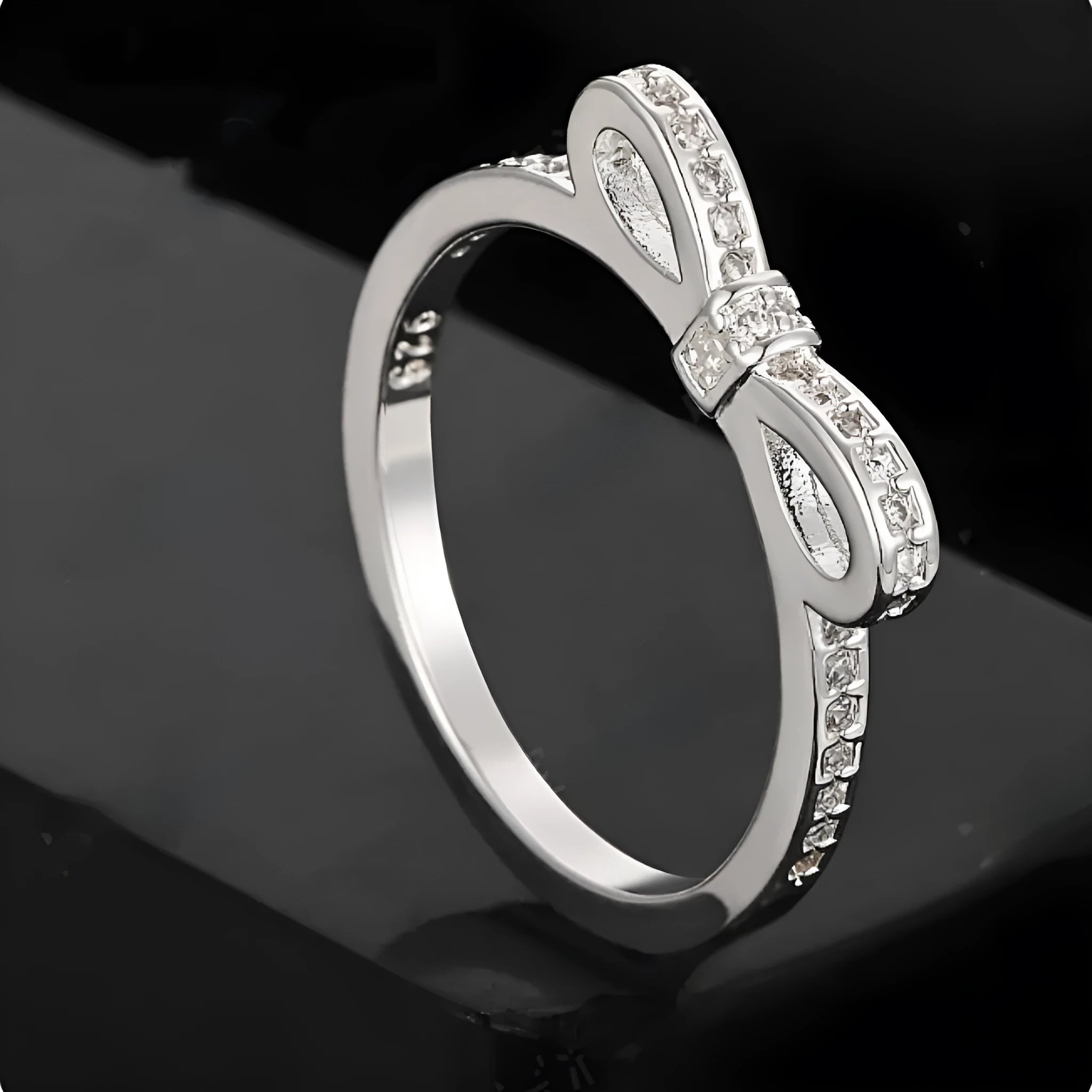 Silver coloured bow-shaped ring with rhinestone and zircon crystal details on a model finger.
