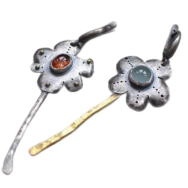 A pair of long retro-style earrings with a geometric floral shape in an asymmetric two-tone colour finish.