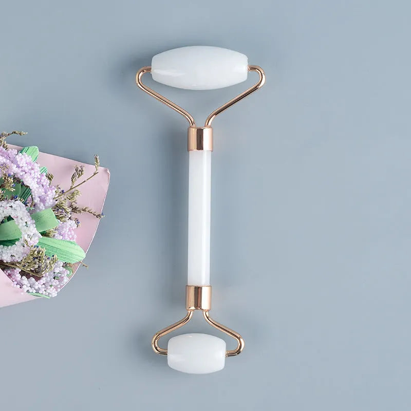 White jade facial roller and gua sha scraping tool set presented on a wooden board.