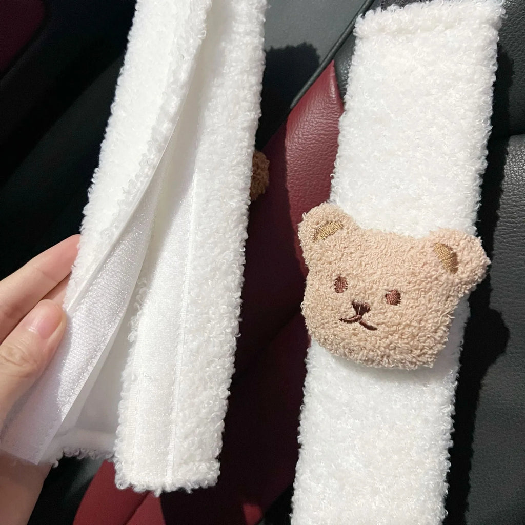 Close-up of a khaki-coloured plush bear seat belt cover on a car seat strap.