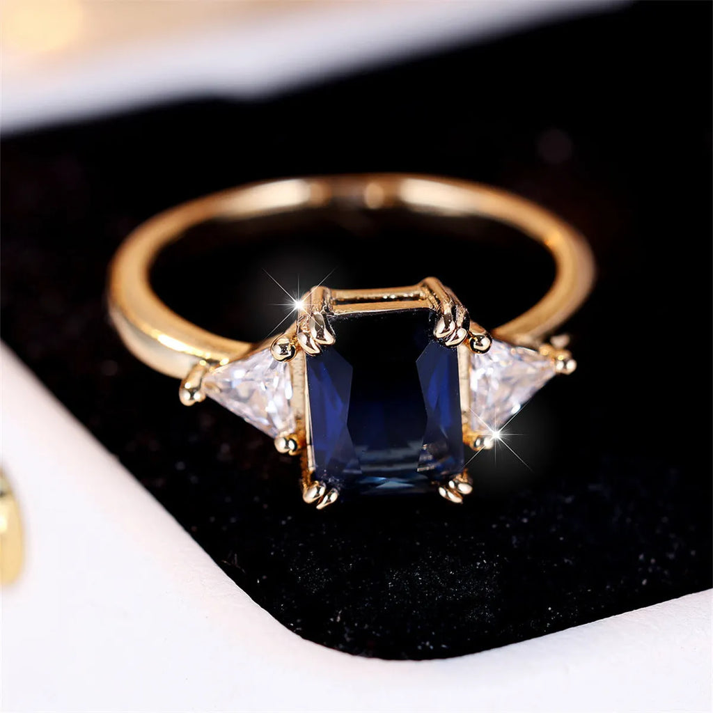 Gold sapphire blue rectangular copper ring for women on a plain background