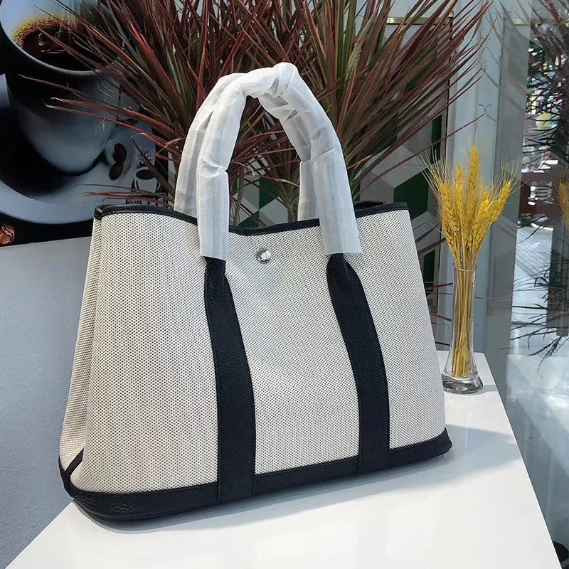 Women's canvas bucket tote bag with leather trim in black colour showing open pocket and crossbody strap