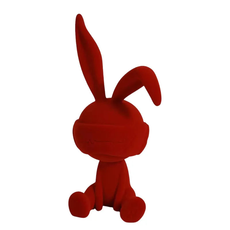 Green resin blindfold rabbit table ornament with suede details on a wooden shelf.