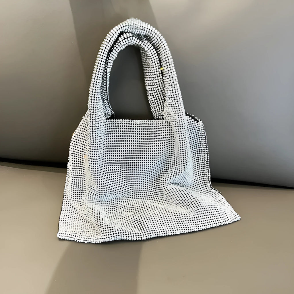 Silver cotton thread evening clutch covered in shiny rhinestones with an open outer pocket and shoulder strap.