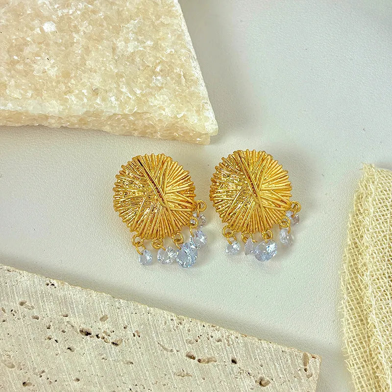A pair of geometric gold metal earrings with round details on a white background.