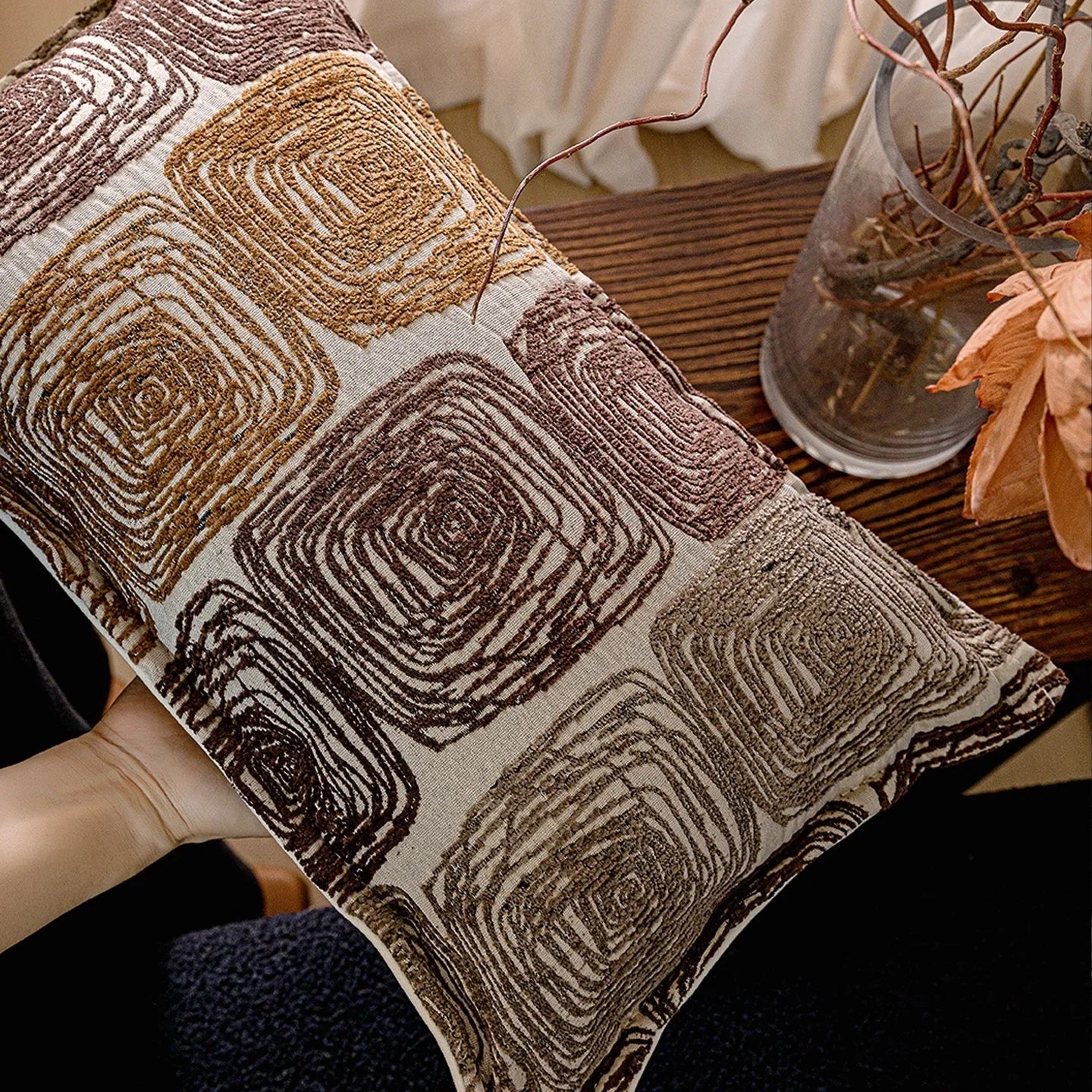 Cream and coffee coloured abstract coil pattern square pillow cover on a grey sofa.