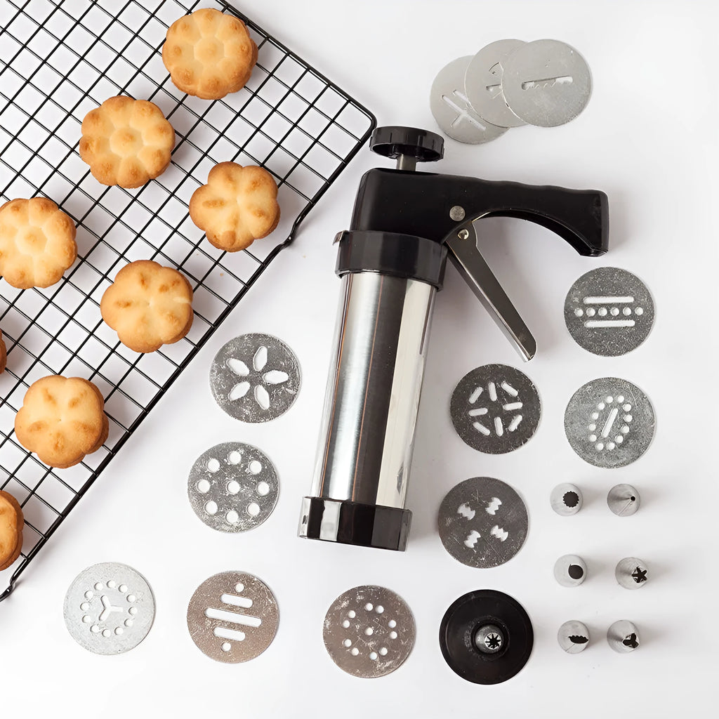 Stainless steel biscuit press gun with assortment of cookie moulds and piping nozzles on a baking sheet.