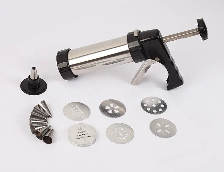 Stainless steel biscuit press gun with assortment of cookie moulds and piping nozzles on a baking sheet.