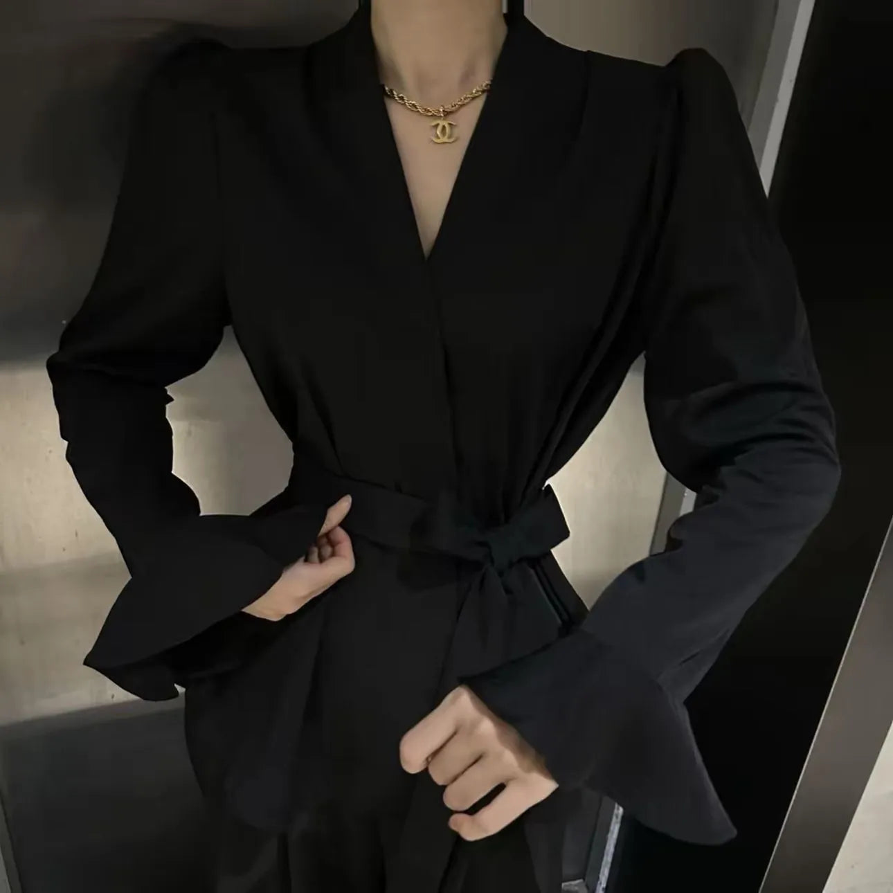 Women's black French-style shirt with an irregular collar and long bell sleeves, showing the tied front detail.