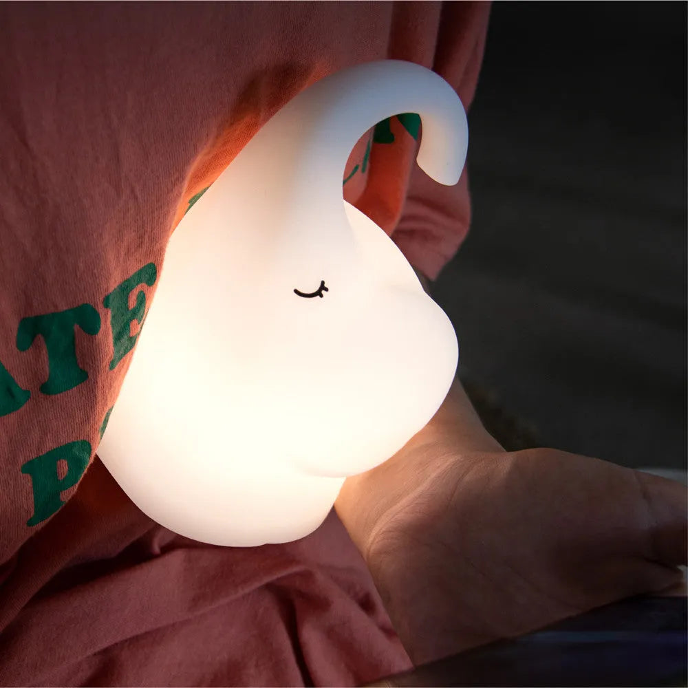 White silicone elephant-shaped night light with a warm glow, placed on a wooden bedside table.