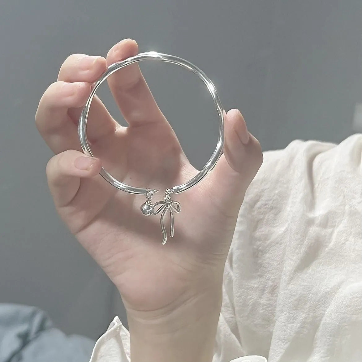 Silver-coloured adjustable bracelet with a bow charm on a wrist.