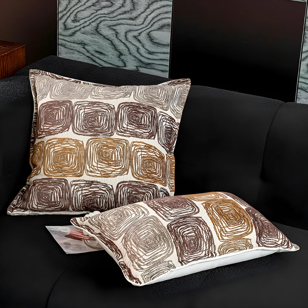 Cream and coffee coloured abstract coil pattern square pillow cover on a grey sofa.