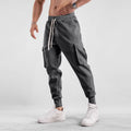 Men's loose beige cotton trousers with an ankle tie and multiple pockets on a casual model.