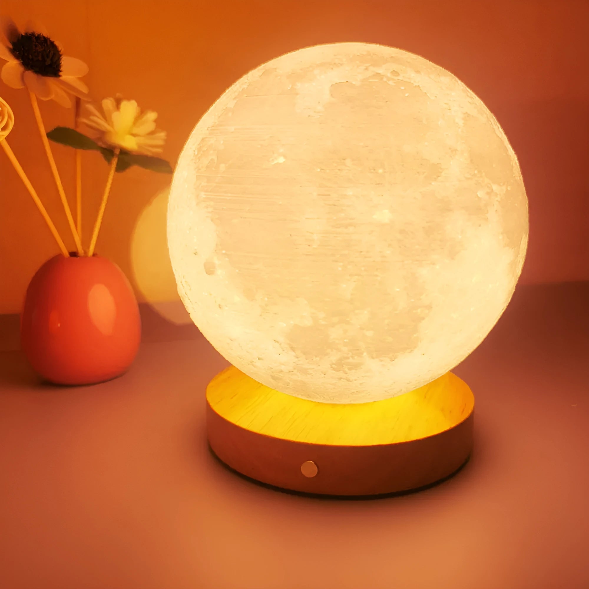 Rotating moon night lamp with wooden base on a table, showing three colour settings and remote control.