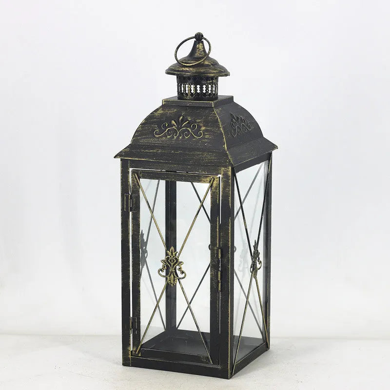 Black and white wrought iron floor standing storm lantern with tempered glass panels on a patio.