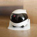 White smart home mobile surveillance robot camera with front sensors on a docking station.