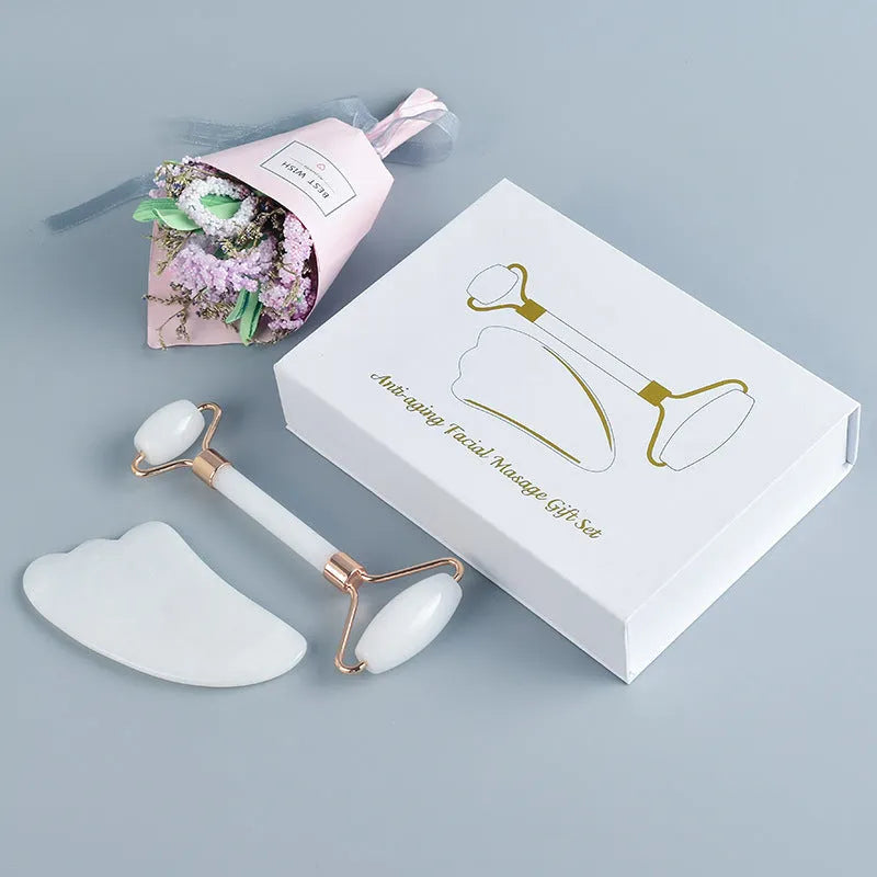 White jade facial roller and gua sha scraping tool set presented on a wooden board.