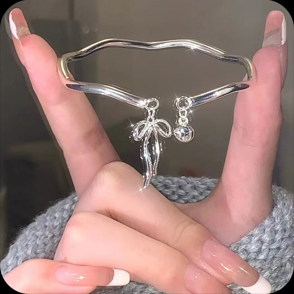 Silver-coloured adjustable bracelet with a bow charm on a wrist.
