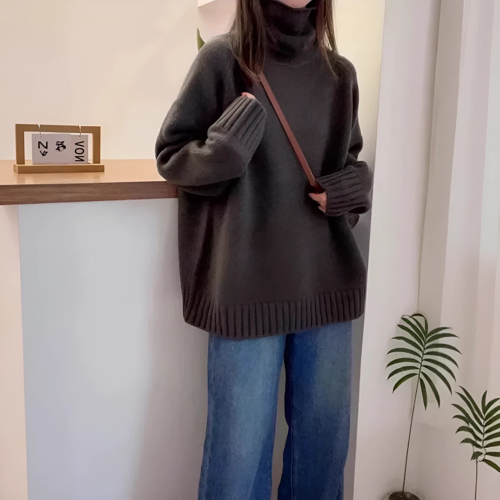 A woman wearing a thick, loose grey turtleneck sweater with a textured curling pile collar.