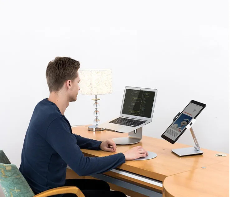 Folding aluminium desktop stand holding a tablet, showing its 360-degree rotation hinge and black/silver colour options.