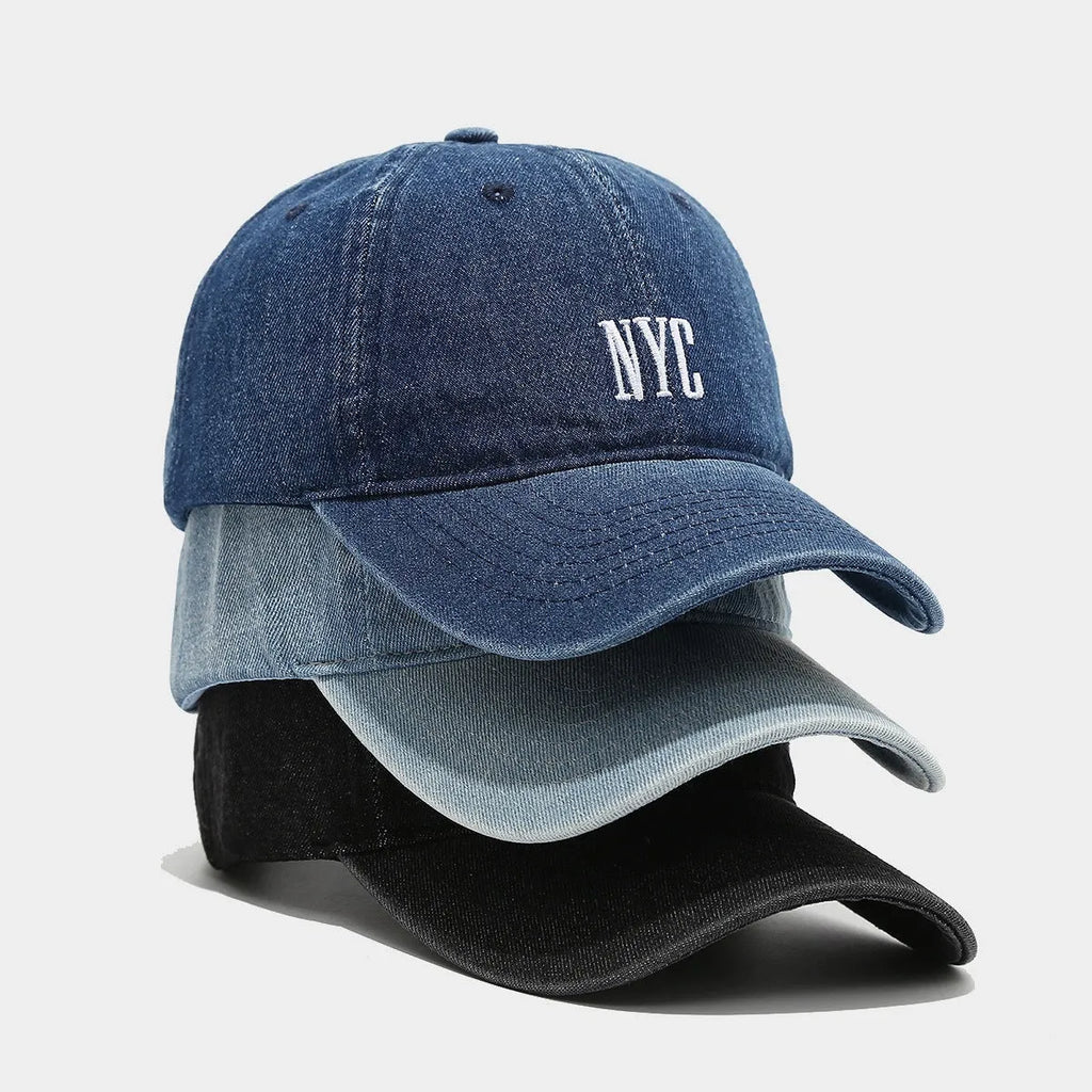 A light blue denim peaked cap with a dome crown, adjustable strap, and decorative white English letters on the front.