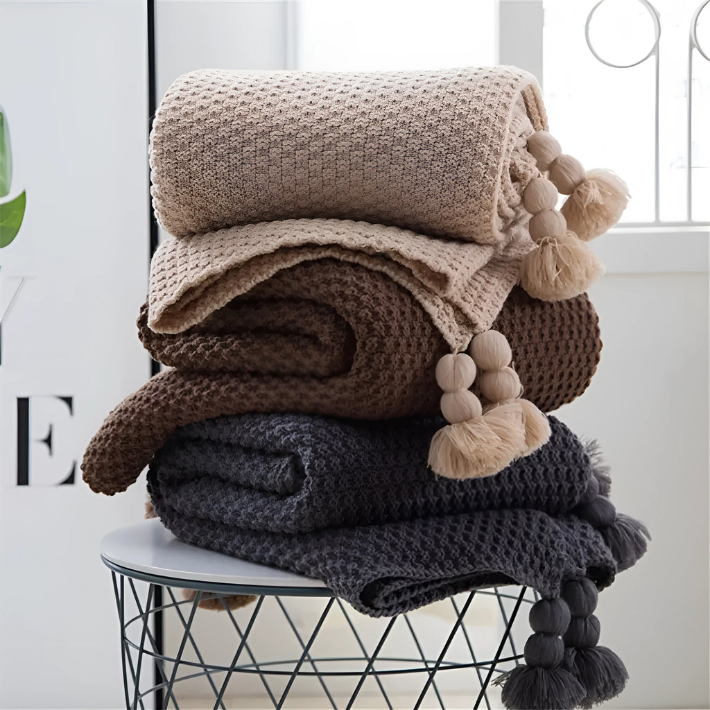 Nordic style fringed knit ball acrylic throw blanket in beige colour on a sofa.