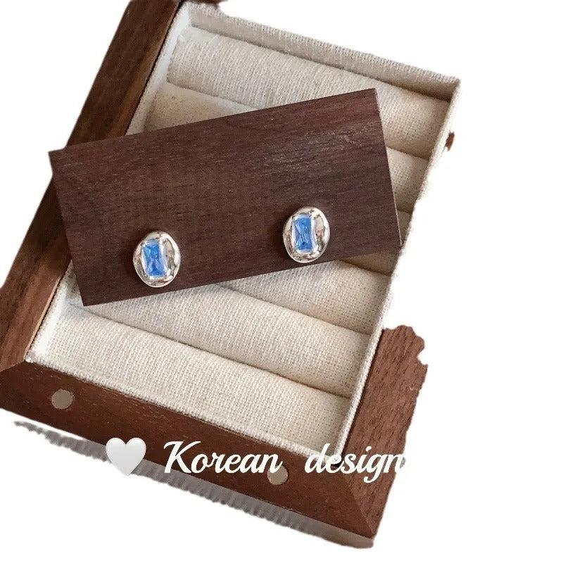 Women's sterling silver oval earrings with heart-wrapped design and blue diamond accents on silver background