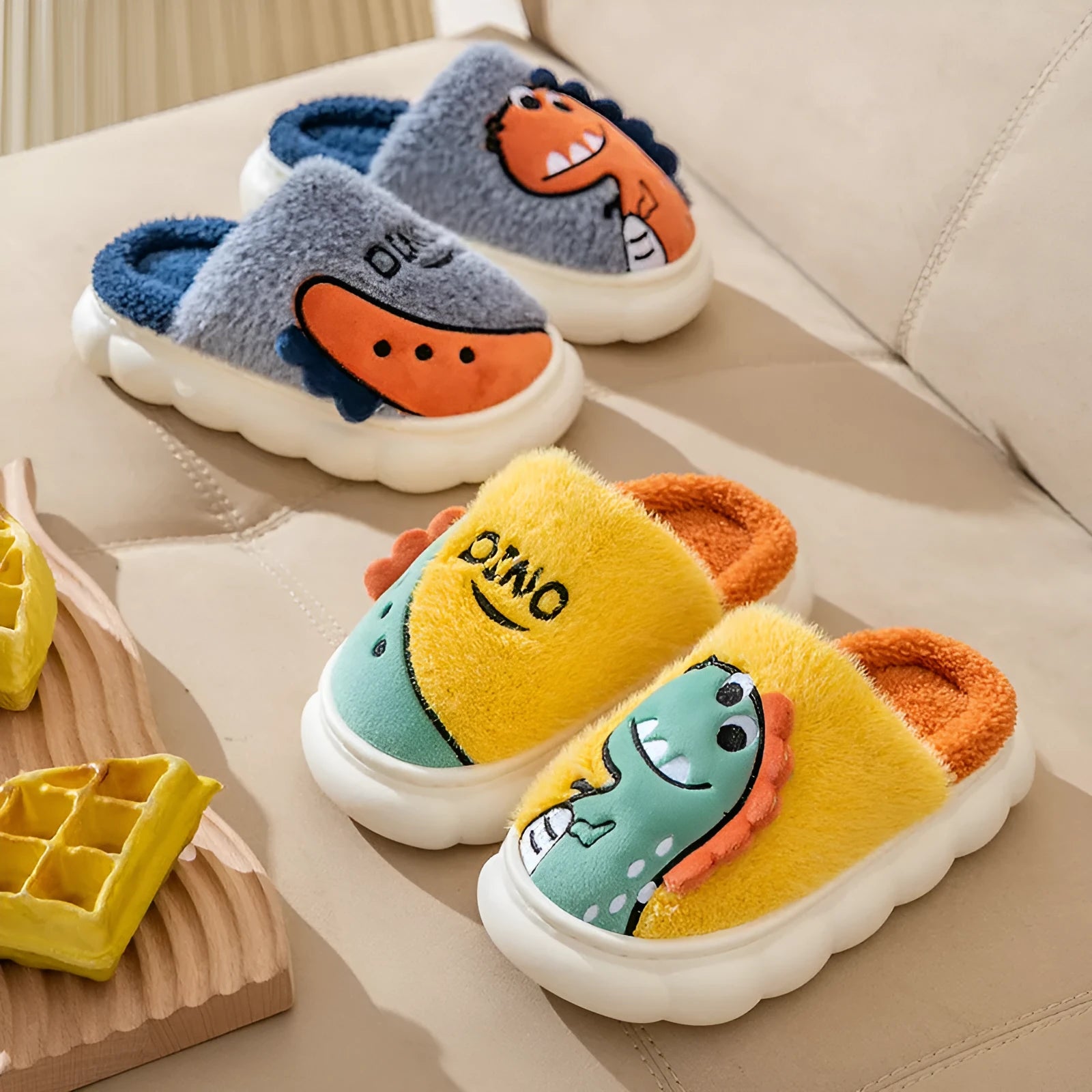 A pair of plush grey dinosaur print slippers with a thickened sole, shown on a wooden floor.