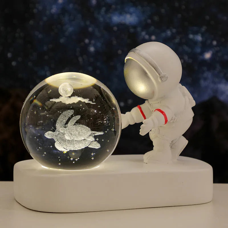 Small clear resin ball night light with glowing astronaut and galaxy scene inside on dark surface