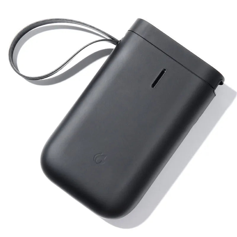 Compact black D11 Bluetooth thermal label printer on a desk next to a smartphone showing the label design app.