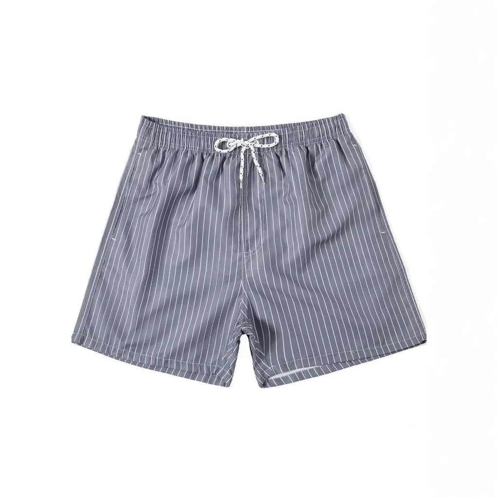 Man wearing navy blue and white striped straight-leg polyester beach shorts on shore.