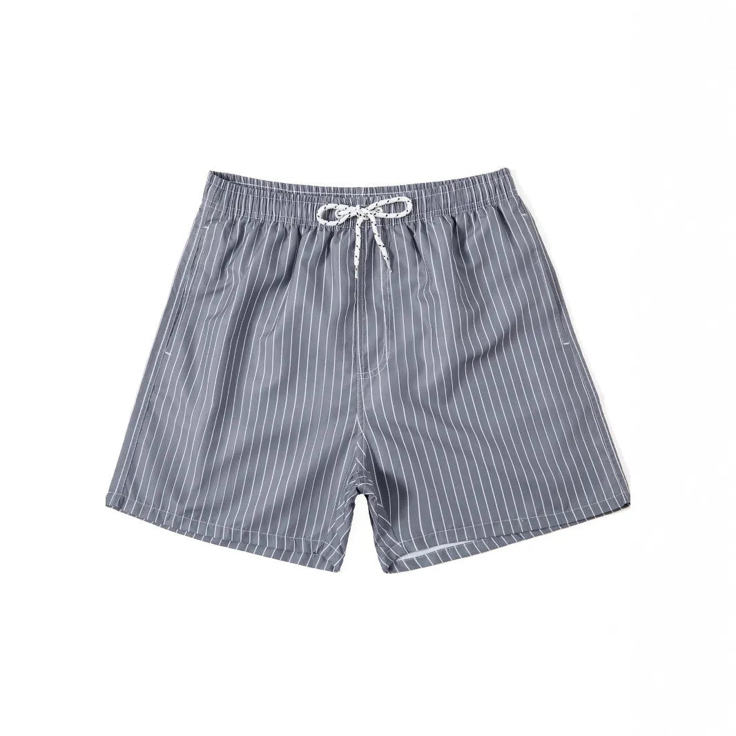 Man wearing navy blue and white striped straight-leg polyester beach shorts on shore.