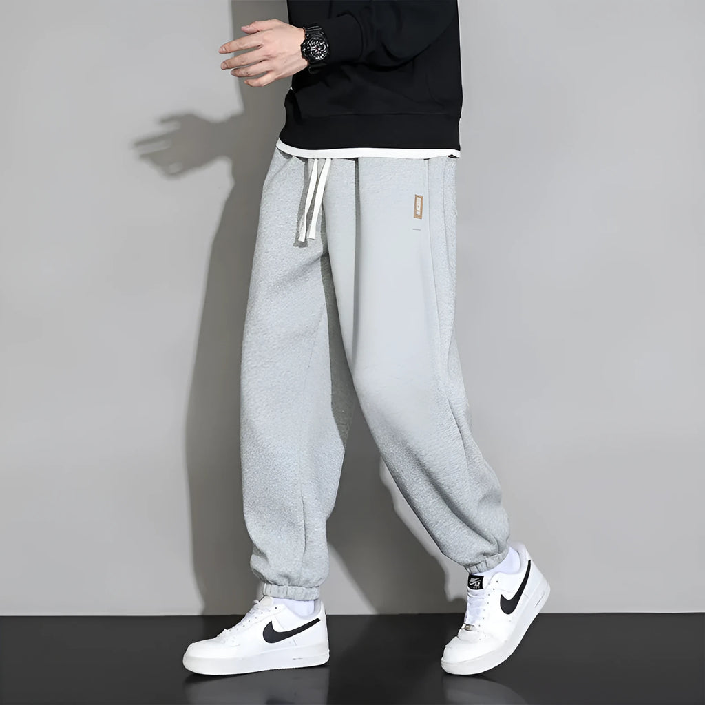 Men's grey loose-fit cotton blend sports trousers with a drawstring waistband on a hanger.