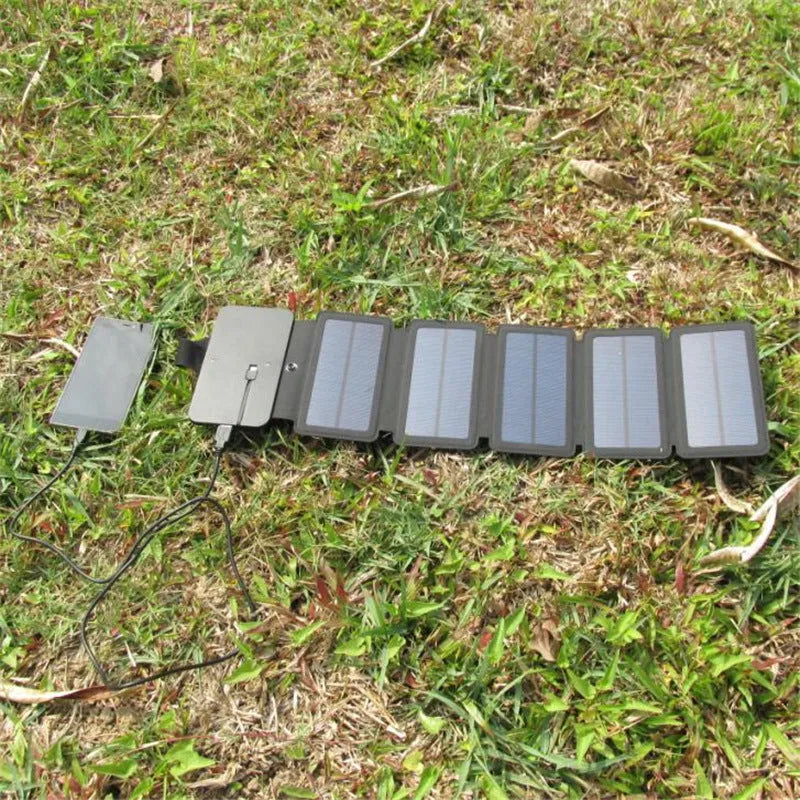 Black folding solar panel charger with monocrystalline cells and USB output, folded flat on a wooden surface, compass buckle visible