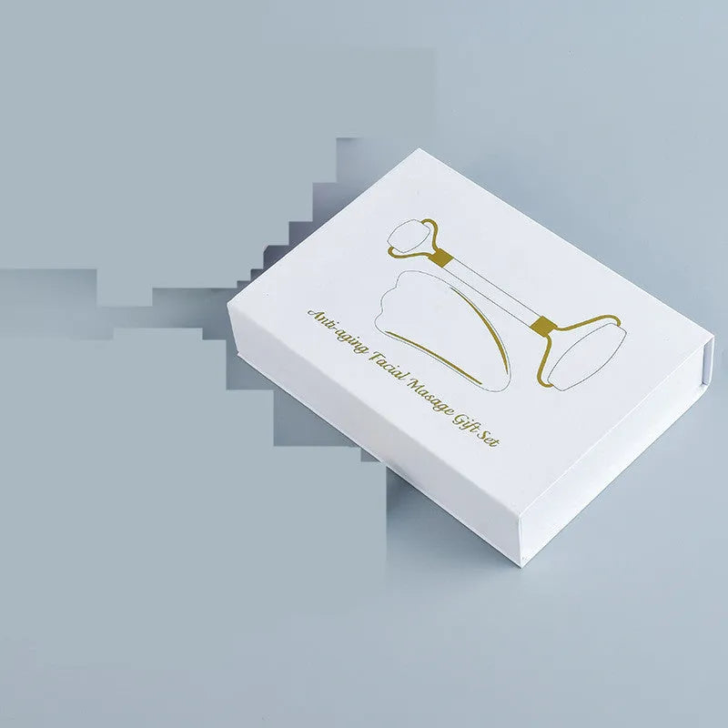 White jade facial roller and gua sha scraping tool set presented on a wooden board.