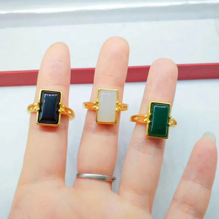 A gold-coloured adjustable ring with a large central green artificial gemstone, showing the national style design.