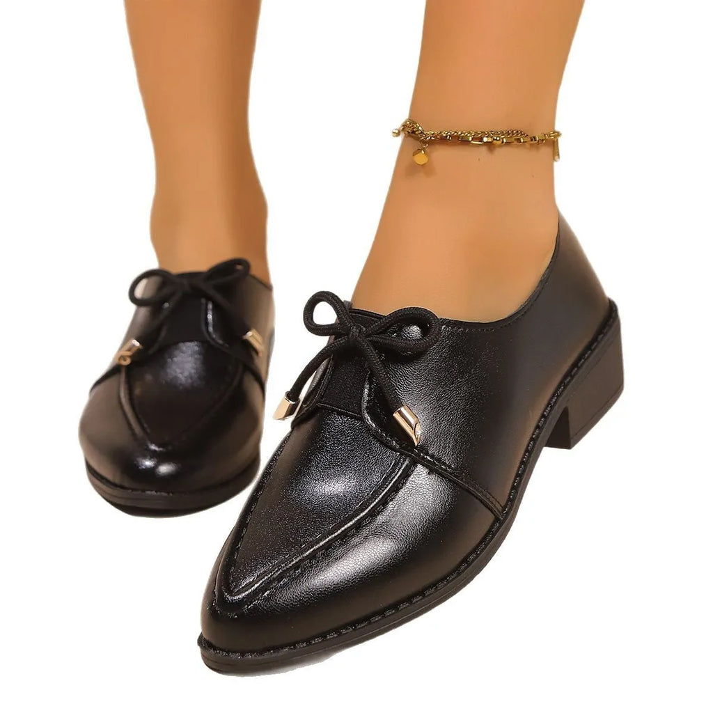 Women's black leather-look flat shoes with a decorative bow on the pointed toe.