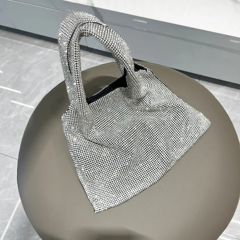 Silver cotton thread evening clutch covered in shiny rhinestones with an open outer pocket and shoulder strap.