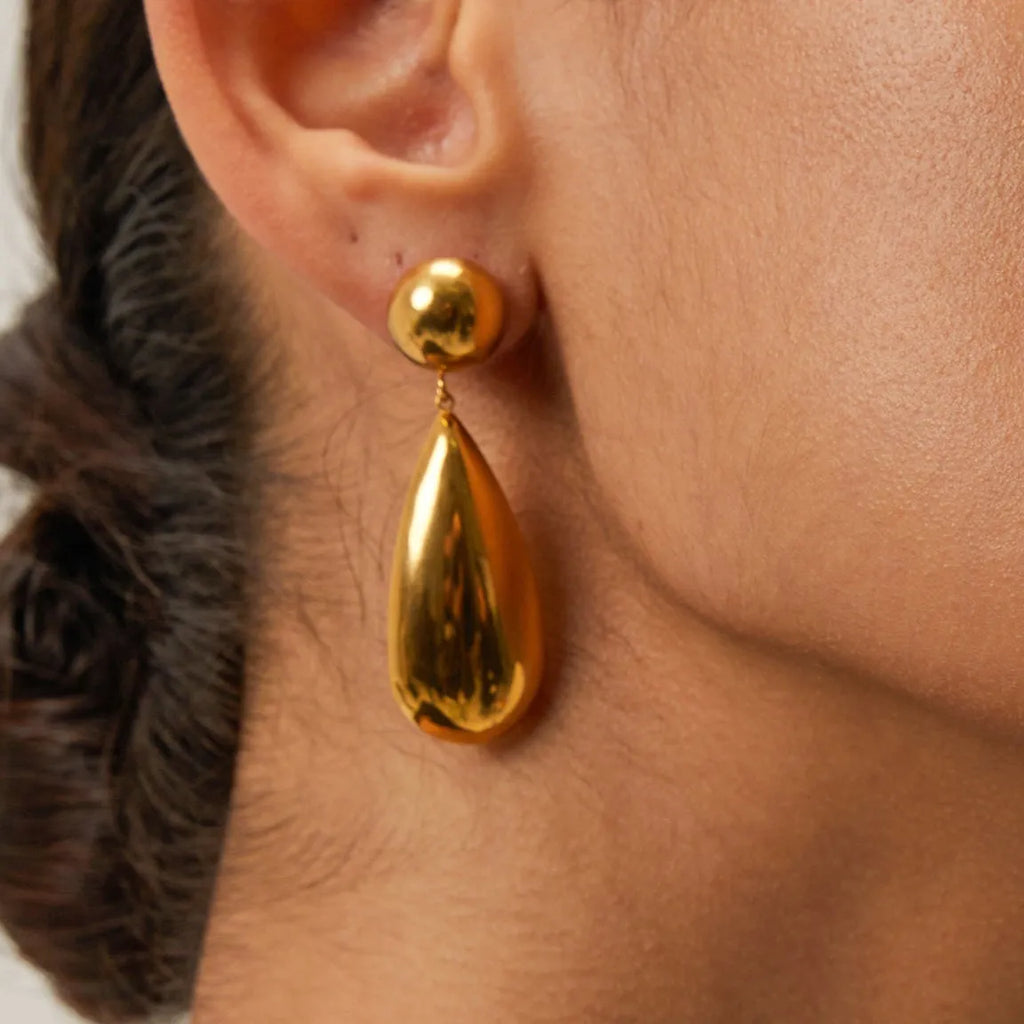 Gold coloured geometric hemisphere earrings with a dangling water drop pendant, made from stainless steel.