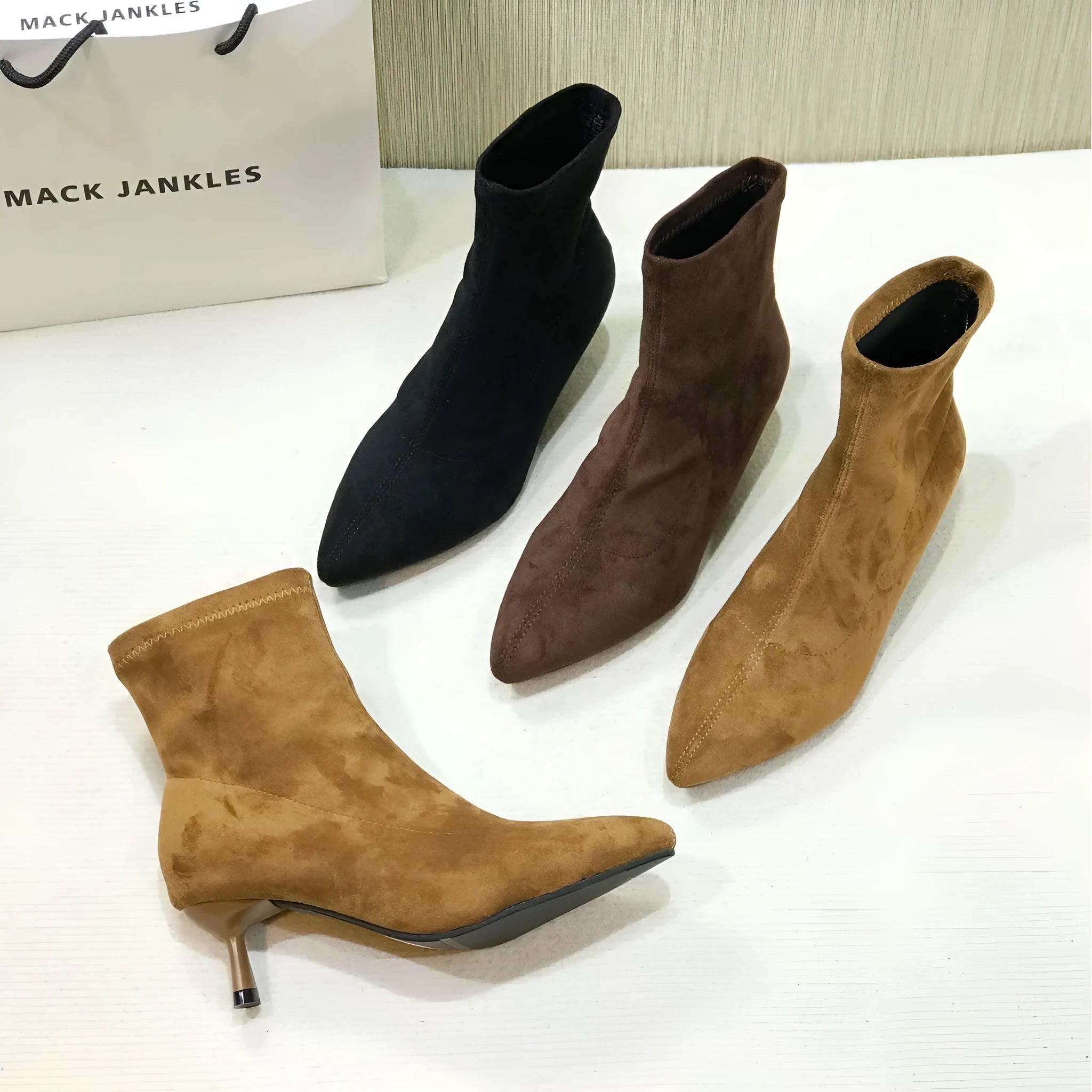 Black microfiber ankle boots with a stiletto heel and pointed toe on a mid-calf sock.