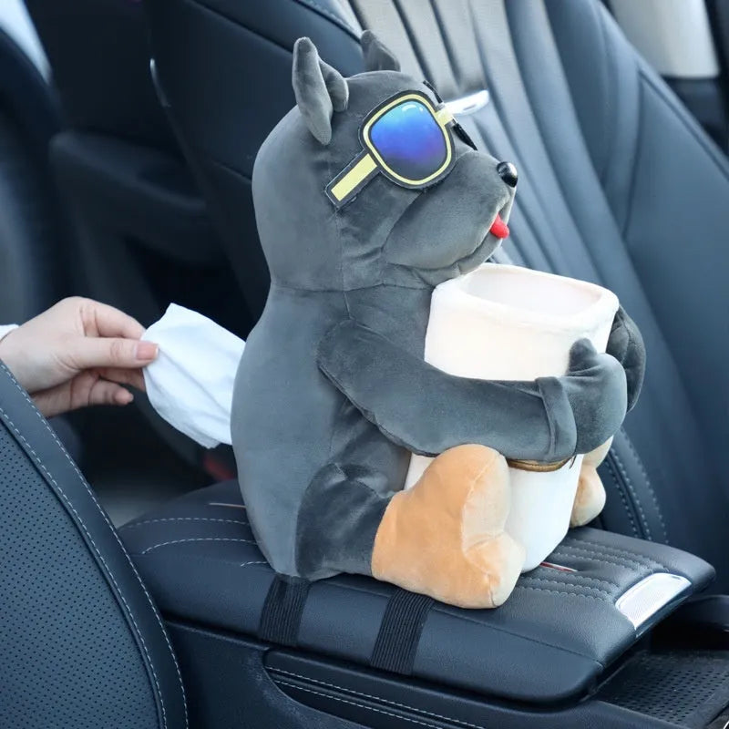 Plush car tissue box holder hanging from flip-down armrest with humorous dog design
