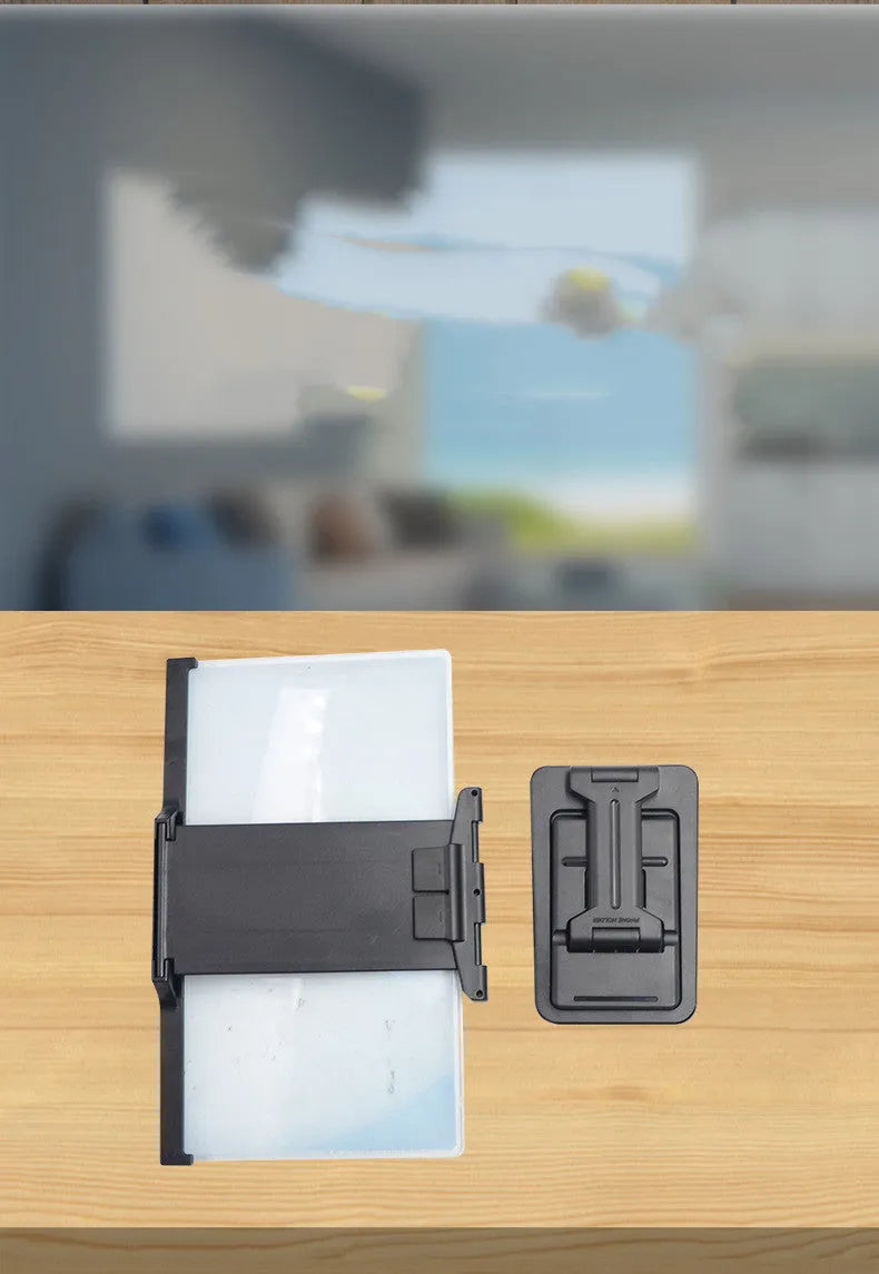 Black foldable mobile phone screen amplifier with a detachable phone holder on a desktop.