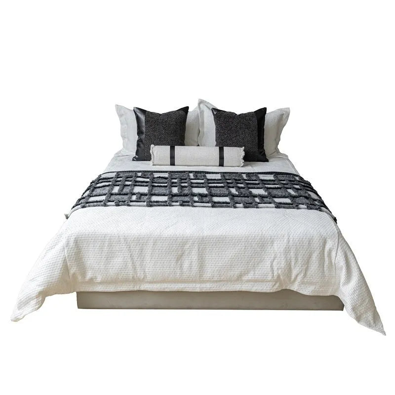 Modern minimalist grey and white plaid bed runner blanket set with a leather round pillow on a bed.
